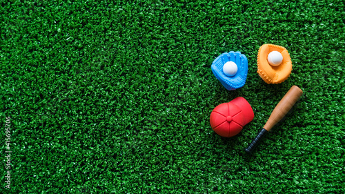 A miniature toy baseball equipment of cap,ball,glove and bat on green grass background with copy space.