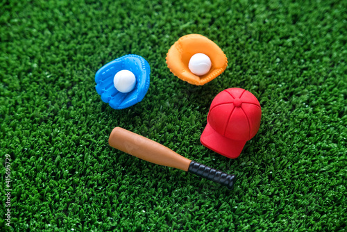 A miniature toy baseball equipment of cap,ball,glove and bat on green grass background. 