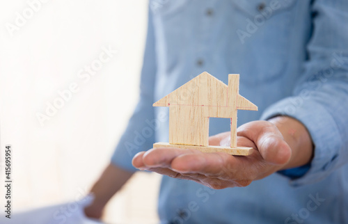 Construction concepts. Hand holding a wooden miniature home, Man hand symbolically holds a mini wood house