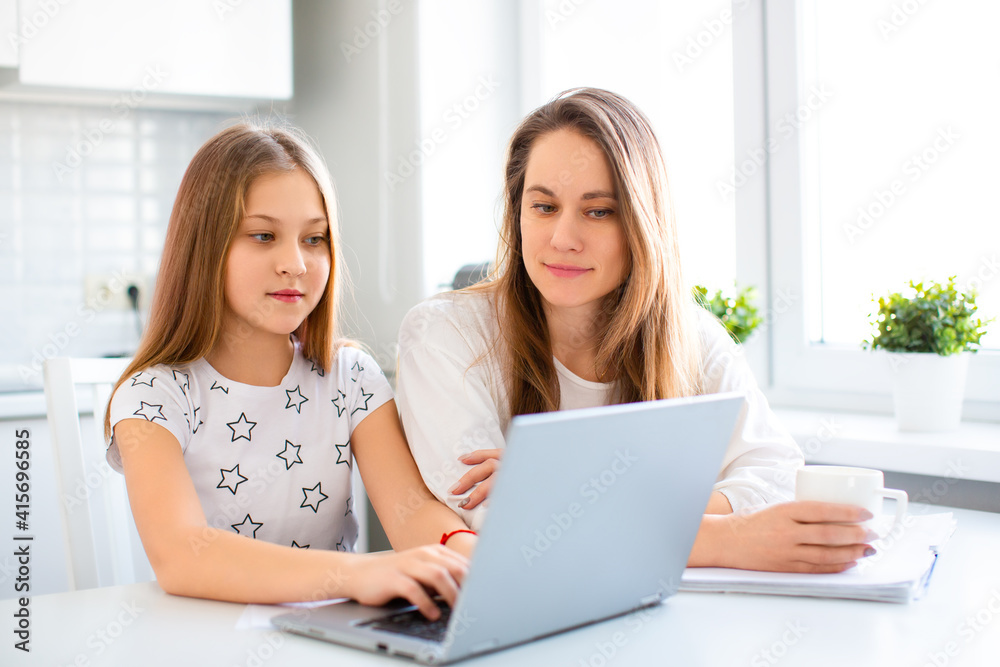 Mom helps her daughter do her homework online. They look at the laptop monitor, where the teacher explains the lesson. Mom helps her daughter do her homework online. They look at the laptop monitor, where the teacher explains the lesson.