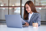 Closeup image of a beautiful young asian business woman drinking coffee and using laptop computer while working in office