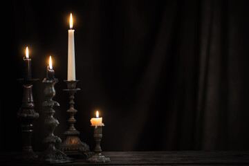 antique candlestick with burning candle on old wooden table on background black velvet curtain