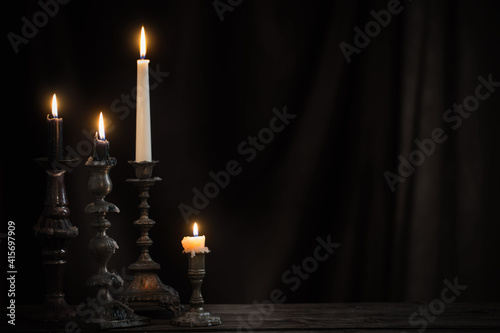 antique candlestick with burning candle on old wooden table on background black velvet curtain