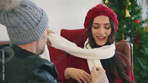 Man and woman couple in casual winter outfit sitting in living room giving a gift putting winter scarf to his lover and celebrate christmas event together with happy and romantic mood
