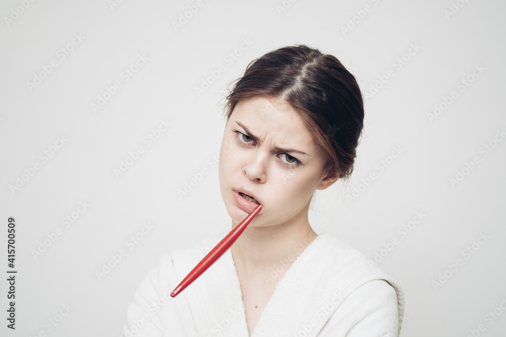woman with a toothbrush in her mouth on a light background and a white robe woman with a toothbrush in her mouth on a light background and a white robe