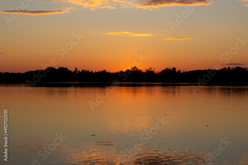 A colorful sunny sunset is reflected on the surface of the calm lake.