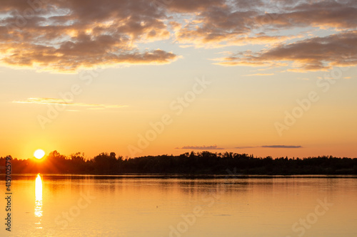 A colorful sunny sunset is reflected on the surface of the calm lake.