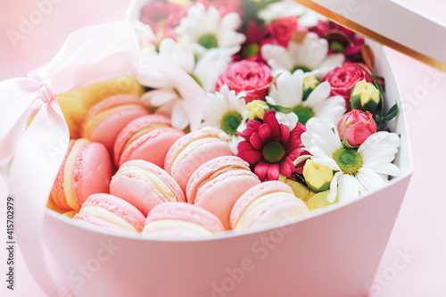 Macarons with flowers of different kinds in a box in the shape of a heart against a pink background. A gift for any occasion