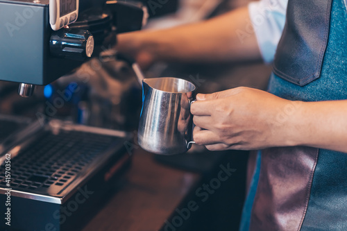 Barista heats milk steam for making lattes at coffee shop.