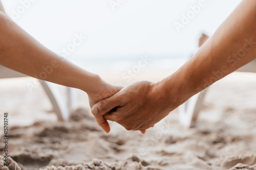 Couple of lovers sitting on beach chair holding hands on the beach in the morning. Newlywed couple on a romantic vacation