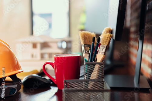 paint brush and pencil in pencil box, cup of coffee and sefty helmet on the table. photo