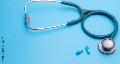 Blue capsule pills and green stethoscope on blue background. Health checkup. Cardiology doctor equipment for heartbeat test. Healthcare and medical concept. Diagnostic medical tool for diagnosis.