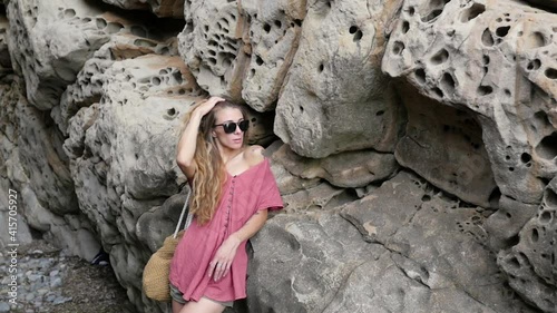 beautiful girl in glasses and with a thermo mug near the rocks. young woman posing next to a rock photo