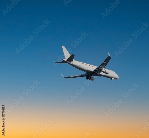 Close up of large passenger airplane flying in beautiful blue and orange sunset sky.