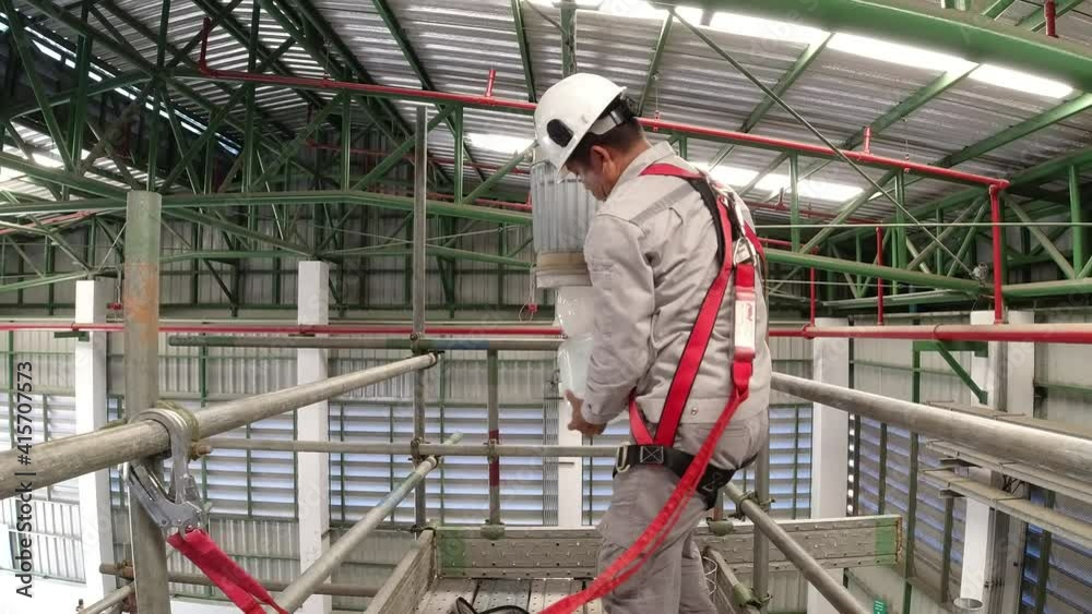 An electrician is working on a steel scaffold to fix the light bulb, wearing safety equipment to prevent falling from a height. 