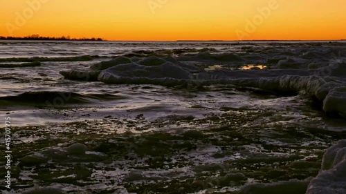 Along the edge of a frozen shoreline, waves lap against the winter ice pack. photo