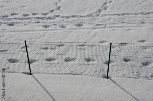 Wire fence with barbed wire. On a snowy meadow is a fence with metal posts and wire mesh. view from above. protective fence of prisons, waterworks, sources of drinking water. Overcoming is difficult