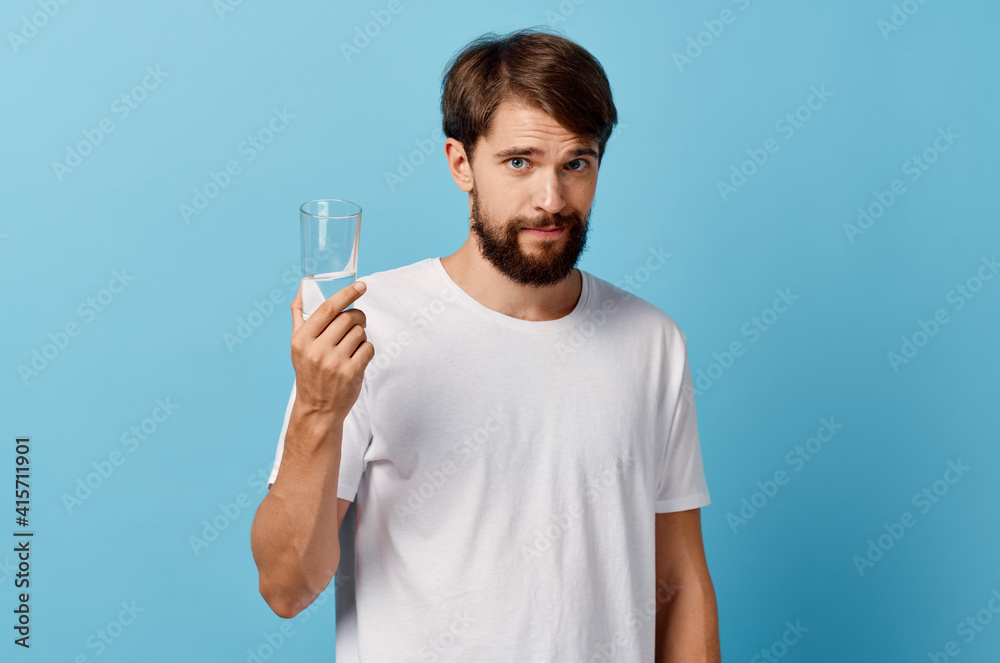 man with beard holding glass of water in hand on blue background white t-shirt model cropped view man with beard holding glass of water in hand on blue background white t-shirt model cropped view