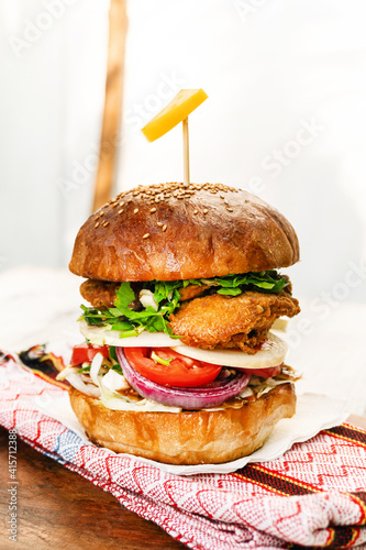 Burger z kurczakiem na jasnym tle, drewnianym stole w świetle dziennym.