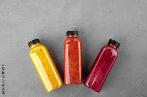 Three plastic bottles with freshly squeezed juice on gray background