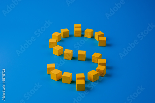 Dollar sign made with yellow wooden blocks on blue background. Currency and finance minimal concept