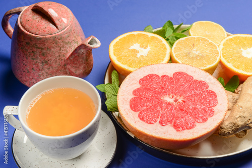 Tea cup and tea pot with cut citrus fruit over blue background. Tea time, healthy lemon and grapefruit drink concept.