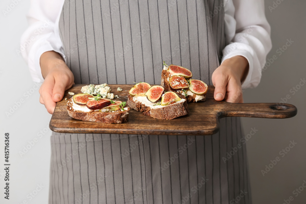 Female chef holding wooden board with tasty sandwiches, closeup