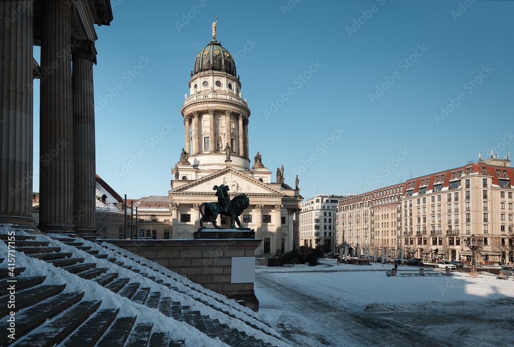 Gendarmenmarkt square in Berlin with French Cathedral, or Franzusischer Dom in German. Picture taken from the steps of Concert Hall on a bright Winter day with blue sky and snow.