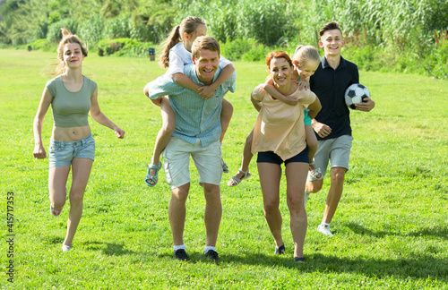 Large family happily playing and running outdoors on green meadow