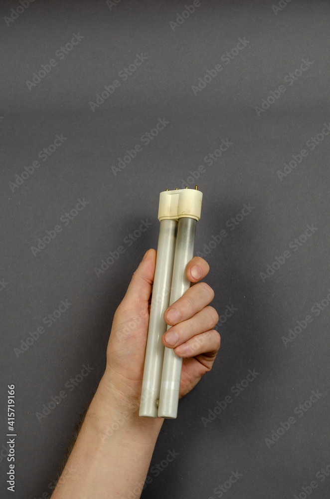 A hand holds a burnt-out fluorescent lamp on a gray background. A hand holds a burnt-out fluorescent lamp on a gray background.