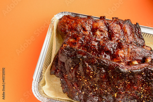 BBQ grilled ribs in a metal tray for delivery. Take out concept, eating at home. In foil delivery box, food take away.