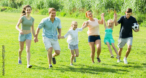 caucasian family happily playing and running together outdoors on green meadow