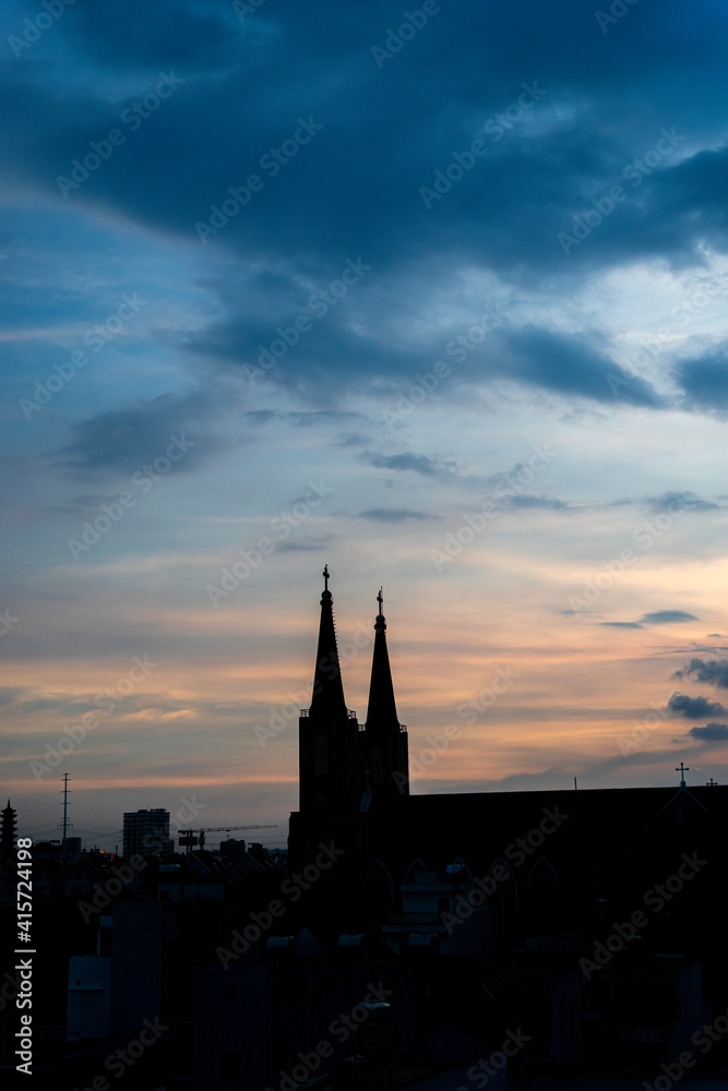 Beautiful red and blue sunrise sky with clouds over black silhouette of city with tower of church on horizon. Silhouette of the catholic church and cross