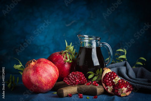 Pomegranate juice in a jug, whole pomegranates and seeds on dark blue background. Dark and moody. photo