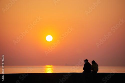 海岸で座って綺麗な夕焼けを見ているカップルの姿