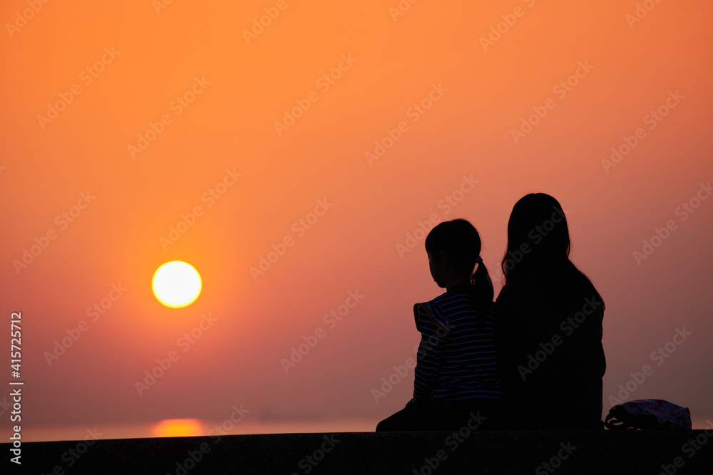 海岸で綺麗な夕焼けを見ている子供姉妹の姿の風景