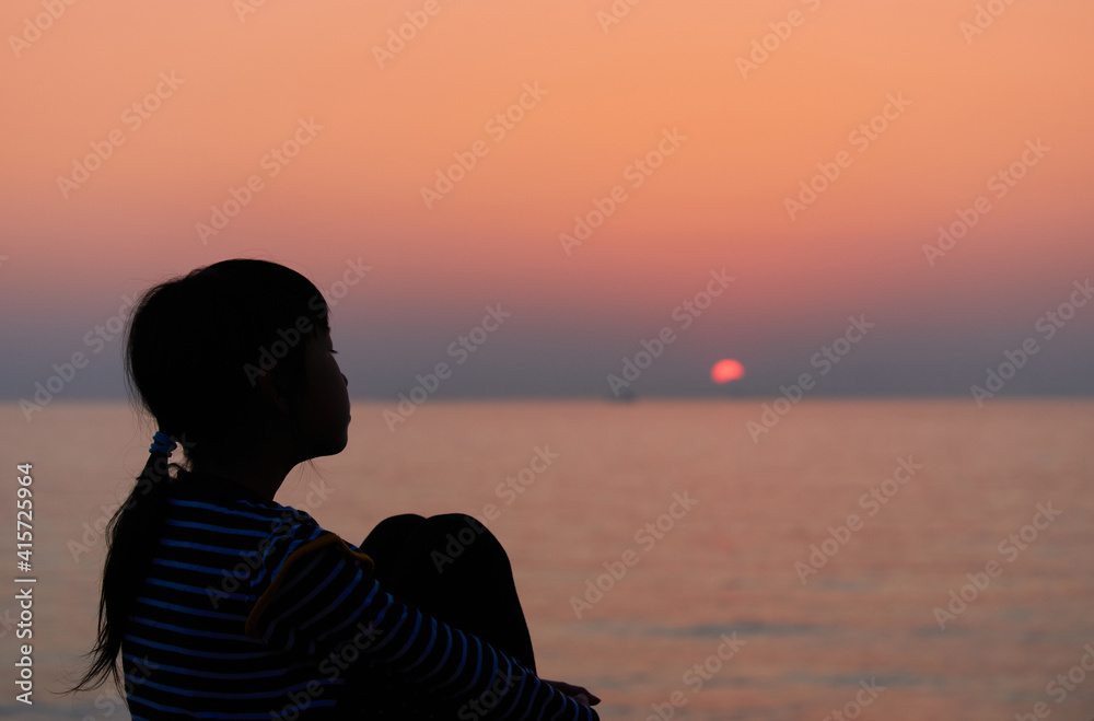 海岸で座って綺麗な夕焼けを見ている可愛い子供の姿