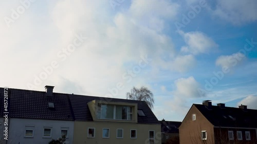 Camera pans up from houses to beautiful blue sky with clouds in sunshine