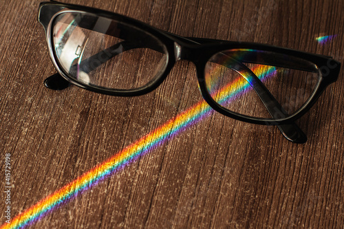 Photochromic glasses on a wooden table crosses a beam of sunlight decomposed into a rainbow spectrum. photo