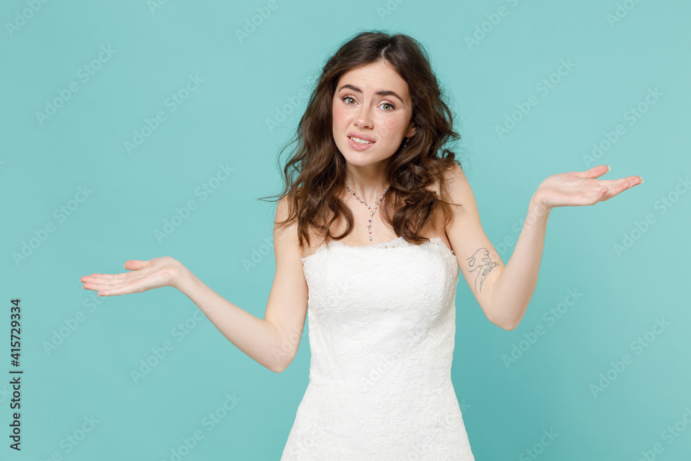 Confused puzzled bride young woman 20s in beautiful white wedding dress spreading hands say oops isolated on blue turquoise color wall background studio portrait. Ceremony celebration party concept. Confused puzzled bride young woman 20s in beautiful white wedding dress spreading hands say oops isolated on blue turquoise color wall background studio portrait. Ceremony celebration party concept.