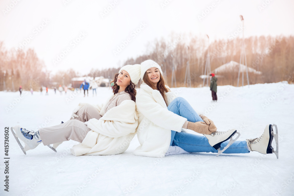 Obraz premium Young happy women in winter with skates on open air ice rink. Girl friendship concept