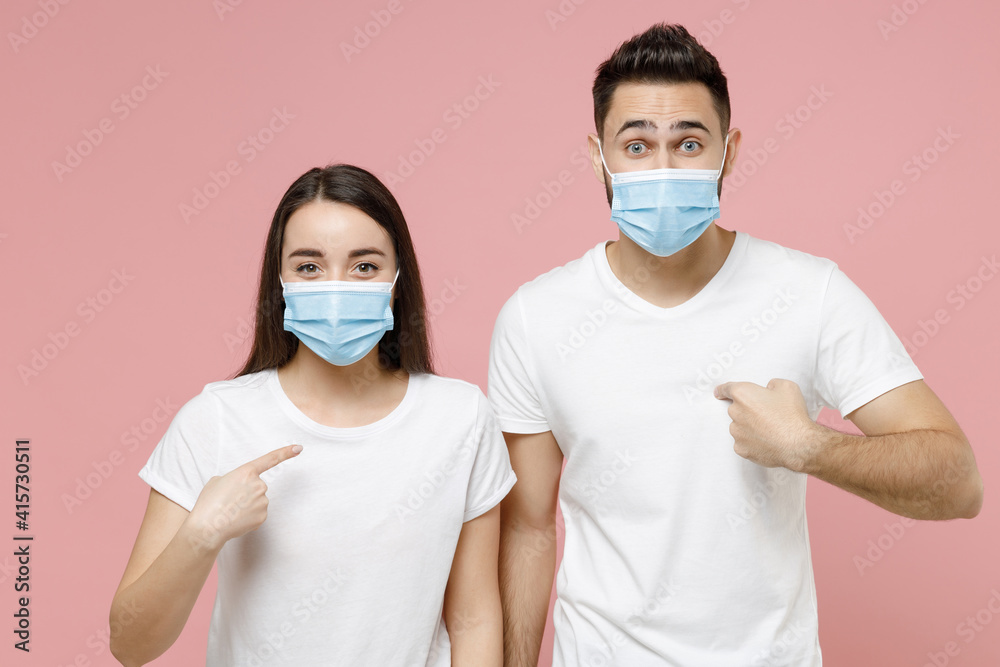 Young couple two friends man woman in white blank print design tshirts sterile face mask to safe from coronavirus virus covid19 on quarantine posing isolated on pastel pink background studio portrait
