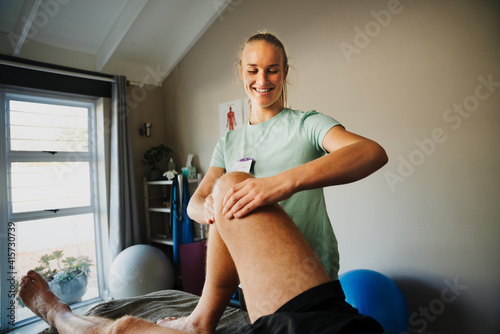 Caucasian physiotherapist massaging injured knee of male patient lying on physio bed in clinic