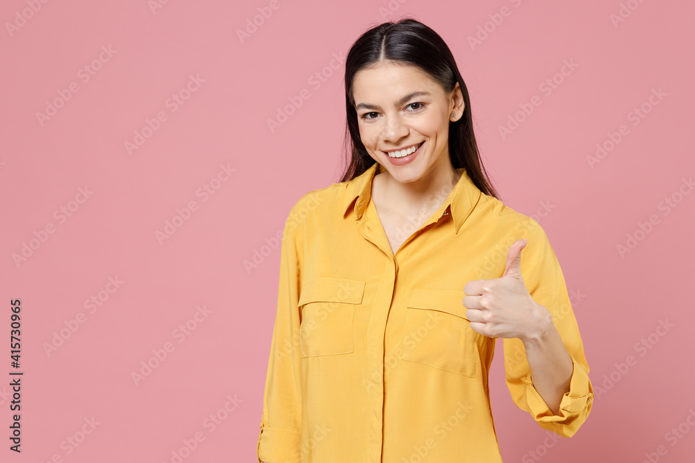 Young smiling happy cheerful friendly satisfied brunette positive cute latin woman 20s wearing yellow casual shirt show thumb up like gesture isolated on pastel pink color background studio portrait. Young smiling happy cheerful friendly satisfied brunette positive cute latin woman 20s wearing yellow casual shirt show thumb up like gesture isolated on pastel pink color background studio portrait.