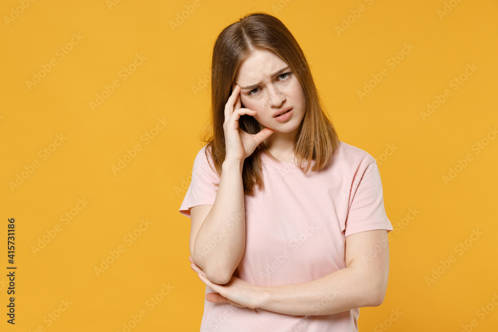 Fototapeta premium Young puzzled thoughtful pensive troubled overthinking caucasian woman 20s wearing casual basic pastel pink t-shirt lookng camera prop up forehead isolated on yellow color background studio portrait.