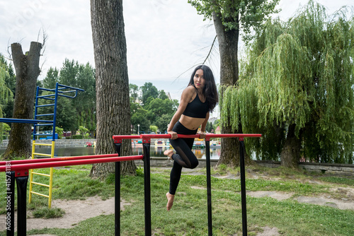 Young female athlete doing exercises on the bar on the street sports field on a sunny day in summer