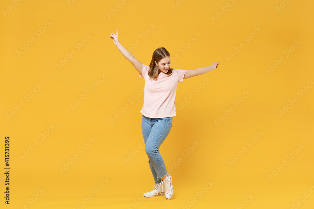 Full length of young happy satisfied woman 20s wearing casual basic pastel pink t-shirt, jeans pointing index fingers outstretching hands celebrating isolated on yellow background studio portrait