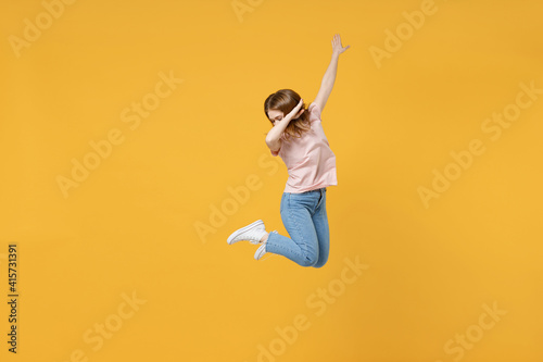 Full length of young expressive woman 20s in basic pastel pink t-shirt jump high do dab hip hop dance hands move gesture youth sign hiding cover face isolated on yellow background studio portrait.