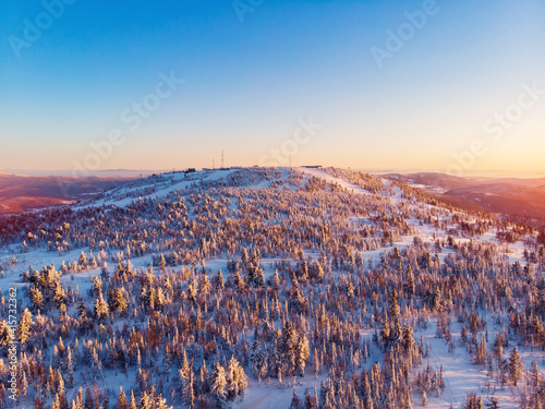 Colorful winter sunset in Sheregesh ski resort mountains with clouds. Aerial top view forest Russia