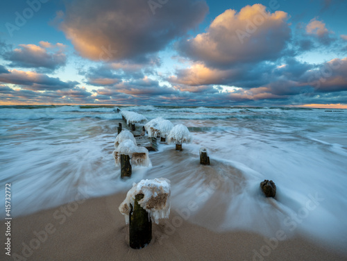 Fototapeta Naklejka Na Ścianę i Meble -  Beautiful winter sea landscape. Ice breakwaters, waves and fiery sunset. Artistic photography..